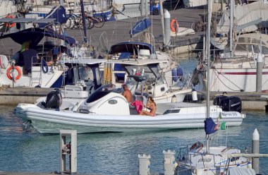 İtalya, Sicilya, Akdeniz, Marina di Ragusa (Ragusa Eyaleti); 28 Haziran 2020, büyük bir kauçuk bot ve limandaki lüks yatlardaki insanlar - EDITORIAL