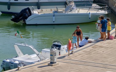 İtalya, Sicilya, Akdeniz, Marina di Ragusa (Ragusa ili); 22 Ağustos 2020, limandaki kauçuk bir tekne ve lüks yatlarda yaşayan insanlar - EDITORIAL