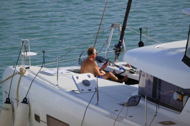 İtalya, Sicilya, Akdeniz, Marina di Ragusa (Ragusa Eyaleti); 2 Eylül 2025, limandaki katamaran yelkenli teknesinde insanlar - EDITORIAL