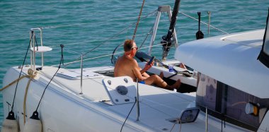 İtalya, Sicilya, Akdeniz, Marina di Ragusa (Ragusa Eyaleti); 2 Eylül 2025, limandaki katamaran yelkenli teknesinde insanlar - EDITORIAL