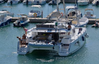 İtalya, Sicilya, Akdeniz, Marina di Ragusa (Ragusa Eyaleti); 14 Eylül 2025, limandaki katamaran yelkenli teknesinde insanlar - EDITORIAL