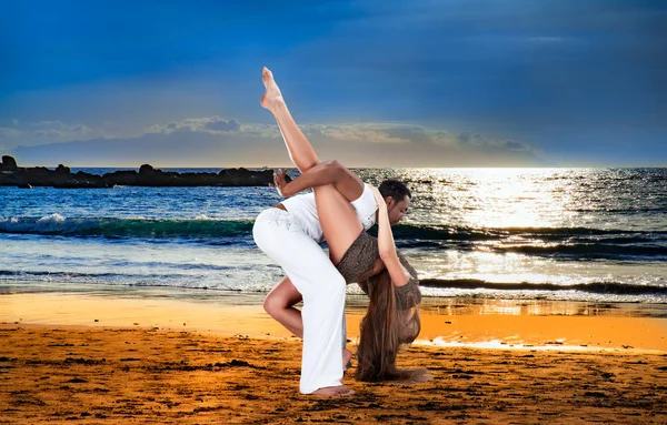 Casal jovem dançando perto do oceano ao pôr do sol — Fotografia de Stock