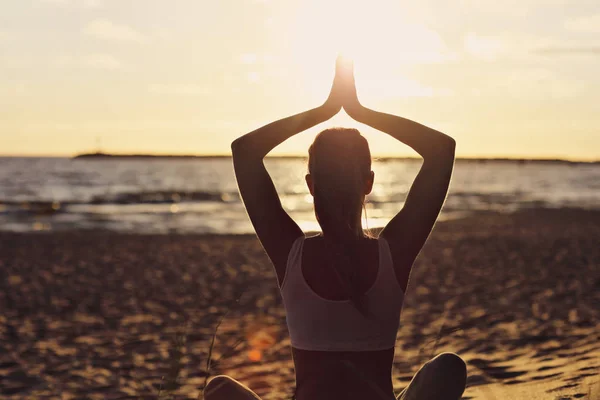 Силует молода жінка практикує йогу на пляжі на заході сонця — стокове фото