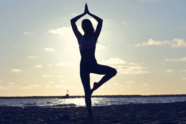 Silhouette jeune femme pratiquant le yoga sur la plage au coucher du soleil — Photo