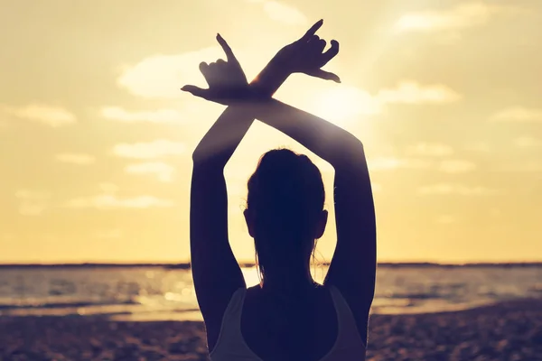 Silhouette jeune femme pratiquant le yoga sur la plage au coucher du soleil — Photo