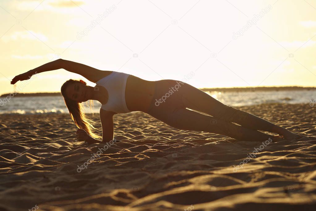 Silhouette young woman practicing yoga on the beach at sunset