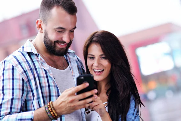 Casal feliz usando smartphone na cidade em dia chuvoso — Fotografia de Stock