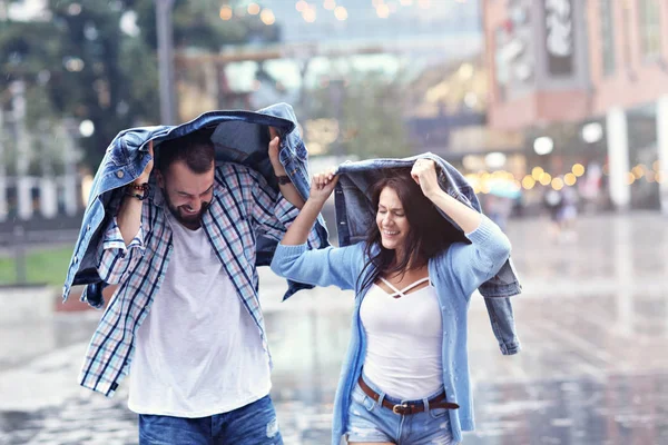 Lyckliga paret kör i regnet i staden — Stockfoto