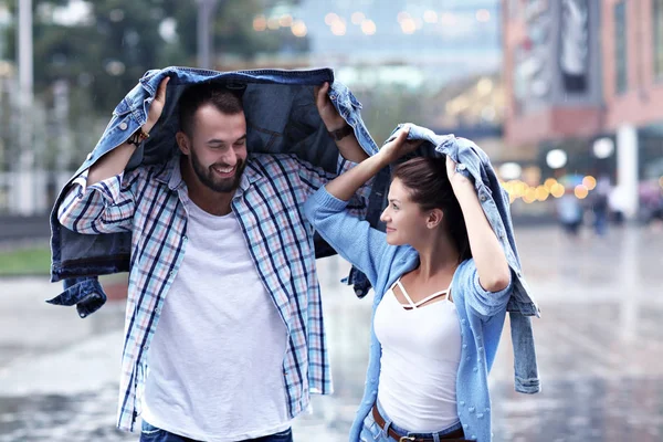 Pareja feliz corriendo bajo la lluvia en la ciudad —  Fotos de Stock