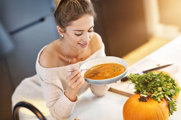 Mulher adulta comendo sopa de abóbora na cozinha — Fotografia de Stock