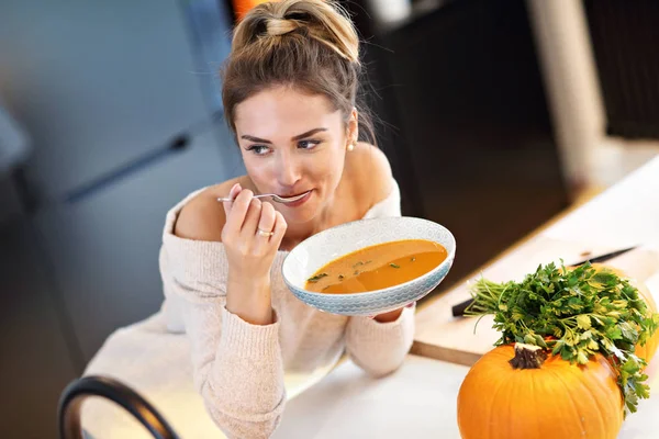Mulher adulta comendo sopa de abóbora na cozinha — Fotografia de Stock