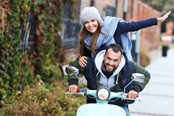 Beautiful young couple smiling while riding scooter in city in autumn — Stock Photo, Image