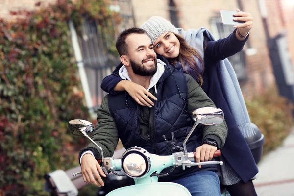 Hermosa pareja joven sonriendo mientras monta scooter en la ciudad en otoño —  Fotos de Stock