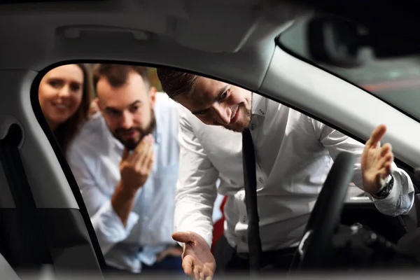 Zeker jonge verkoper auto functies uit te leggen aan de jonge aantrekkelijke eigenaren — Stockfoto