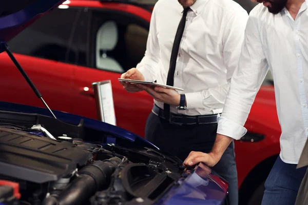 Joven vendedor confiado explicando las características del coche a los propietarios atractivos jóvenes —  Fotos de Stock