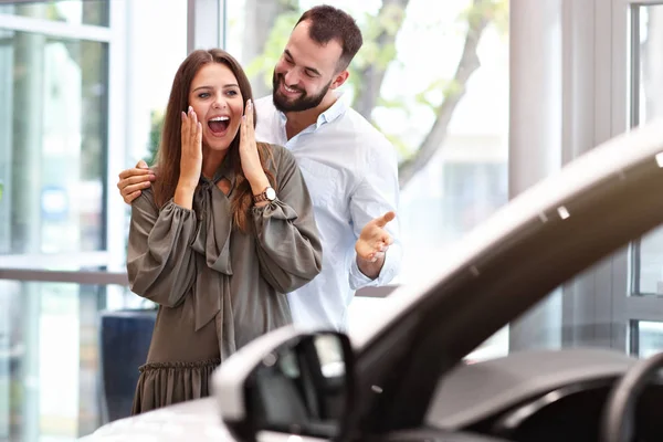 Uomo adulto che fa sorpresa alla bella donna nello showroom dell'auto — Foto Stock