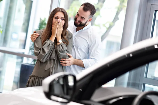 Uomo adulto che fa sorpresa alla bella donna nello showroom dell'auto — Foto Stock