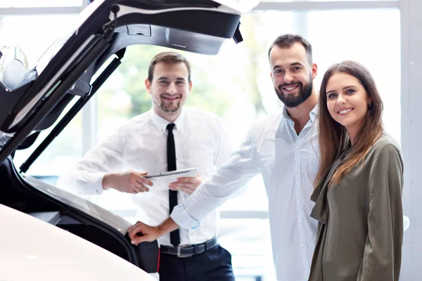 Confident young salesman explaining car features to the young attractive owners — Stock Photo, Image