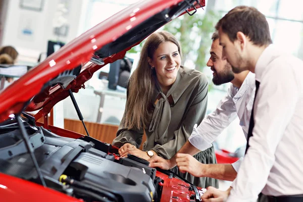 Confident young salesman explaining car features to the young attractive owners — Stock Photo, Image