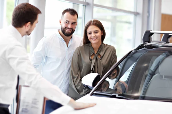 Fiducioso giovane venditore spiegando caratteristiche auto ai giovani proprietari attraenti — Foto Stock