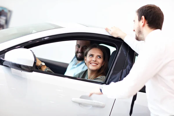 Fiducioso giovane venditore spiegando caratteristiche auto ai giovani proprietari attraenti — Foto Stock