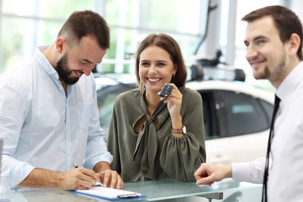 Fiducioso giovane venditore spiegando caratteristiche auto ai giovani proprietari attraenti — Foto Stock