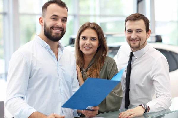 Fiducioso giovane venditore spiegando caratteristiche auto ai giovani proprietari attraenti — Foto Stock