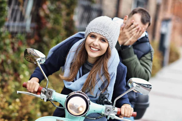 Beautiful young couple smiling while riding scooter in city in autumn — Stock Photo, Image