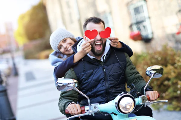 Belo jovem casal segurando corações enquanto andava de scooter na cidade no outono — Fotografia de Stock