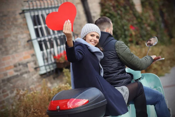 Belo jovem casal segurando corações enquanto andava de scooter na cidade no outono — Fotografia de Stock