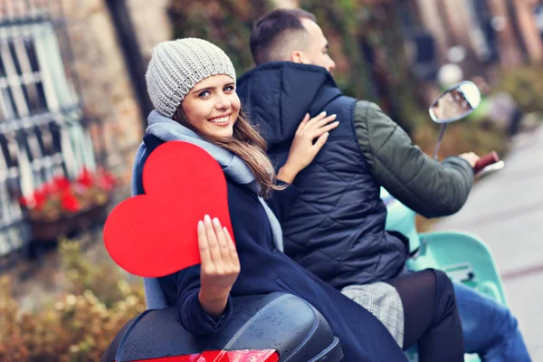 Hermosa pareja joven sosteniendo corazones mientras monta scooter en la ciudad en otoño — Foto de Stock