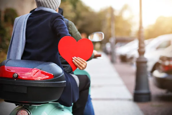 Belo jovem casal segurando corações enquanto andava de scooter na cidade no outono — Fotografia de Stock