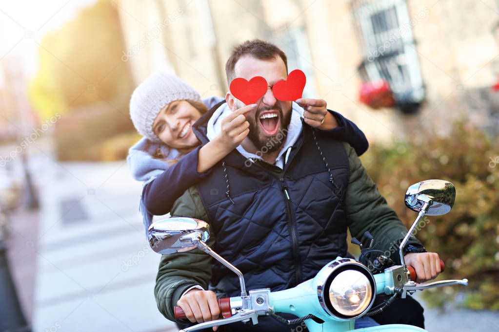 Beautiful young couple holding hearts while riding scooter in city in autumn