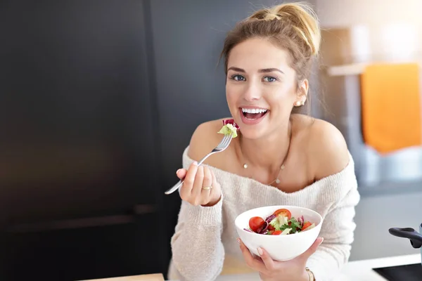 Mulher sorridente bonita comendo salada vegetariana orgânica fresca na cozinha moderna — Fotografia de Stock