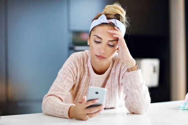 Cansada mujer milenaria descansando cabeza en la cocina y utilizando el teléfono inteligente — Foto de Stock