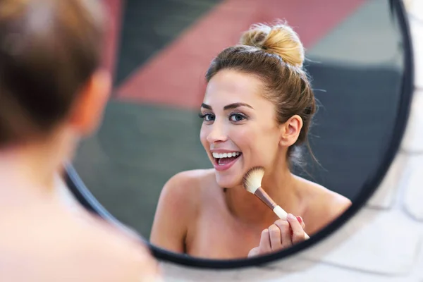 Jonge vrouw toepassing van make-up met penseel in badkamer — Stockfoto