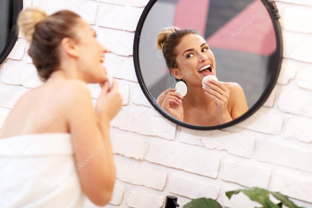 Young woman cleaning face in bathroom mirror