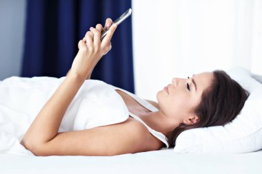 Genç güzel kadın yatakta smartphone ile dinlenme