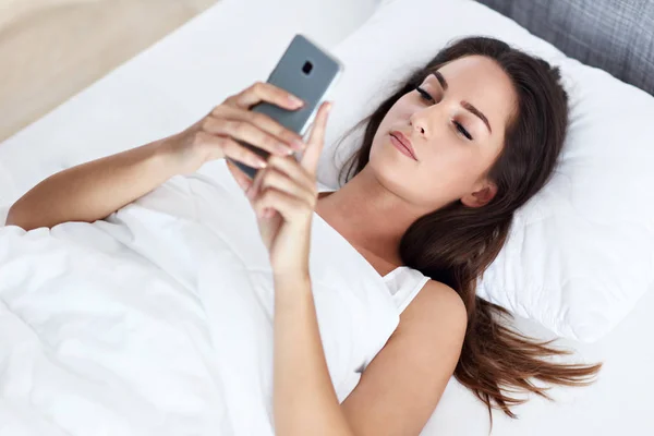 Молодая красивая женщина отдыхает в постели со смартфоном — стоковое фото
