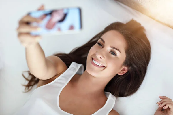 Jonge mooie vrouw wakker in haar bed volledig uitgerust en houdend selfie — Stockfoto