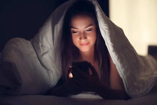 Mooie jongedame rusten in bed met smartphone — Stockfoto