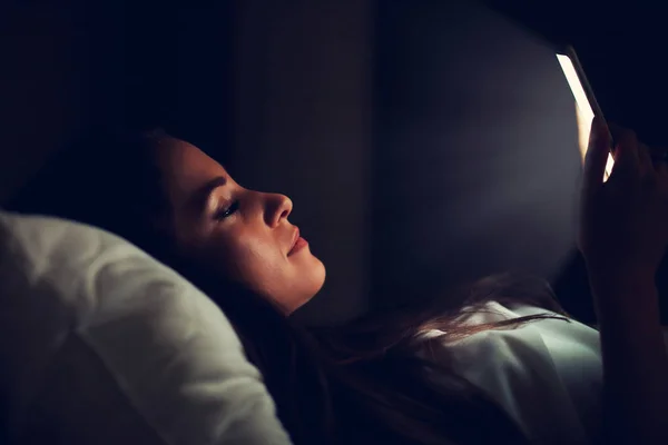 Mooie jongedame rusten in bed met smartphone — Stockfoto