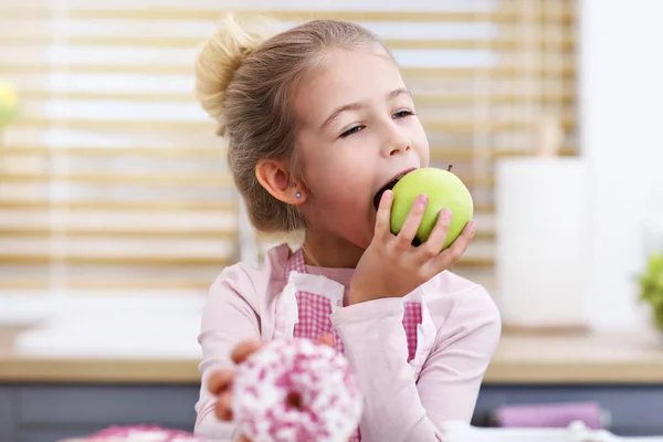 Carina la bambina che sceglie tra mela e ciambella in cucina — Foto Stock