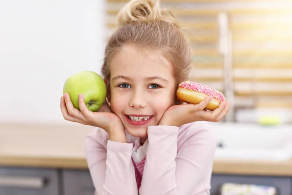 Schattig klein meisje kiezen tussen apple en donut in de keuken — Stockfoto