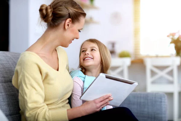 小女孩和她的妈妈坐在家里的沙发上使用平板电脑 — 图库照片