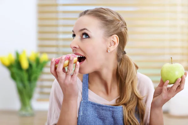 Vuxen kvinna att välja mellan apple och donut i köket — Stockfoto