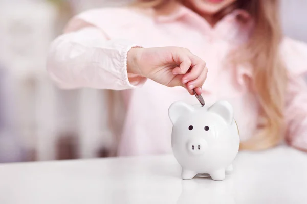 テーブルに座って piggybank を持つ少女 — ストック写真