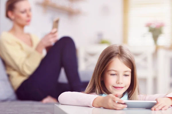 Ung mamma och hennes lilla dotter med smartphone och sitter på soffan hemma — Stockfoto