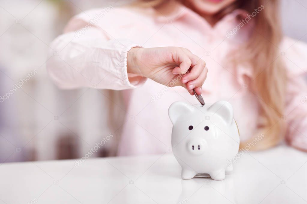 Young girl with piggybank sitting at table