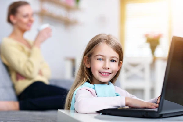 Ung mamma och hennes lilla dotter använder laptop och sitter på soffan hemma — Stockfoto